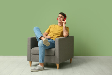 Wall Mural - Handsome young man in headphones listening to music on armchair against green background