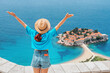 © EdNurg - A female traveler in Montenegro, enjoying a luxurious vacation with panoramic views of Sveti Stefan and the coastal mountains.