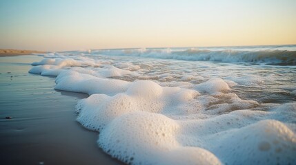 Wall Mural - Gentle sea foam froths over a sandy beach as the sun sets, capturing nature's serene beauty and a moment of coastal tranquility.