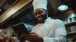 © Iaroslav - Cheerful chef using a digital tablet in a busy professional kitchen, embracing technology for culinary innovation