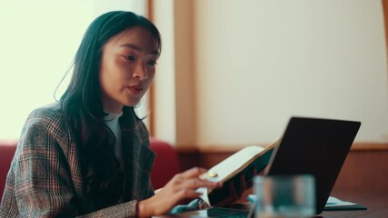 Aufkleber - Young professional woman works remotely, taking notes in a notebook while engaging in a video call on her laptop. Focused and organized, she balances tasks in a modern workspace