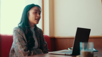 Aufkleber - Young professional woman sits at a table, smiling and gesturing during a video call on her laptop. Engaging in conversation, she enjoys the connection while working remotely