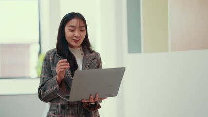 Aufkleber - Young businesswoman presents confidently while holding a laptop. Standing and gesturing with her free hand, she engages the audience in a professional setting