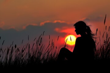 Poster - Sunset silhouette of a woman sitting on a grassy hill against a vibrant orange sky, capturing a moment of tranquility and reflection