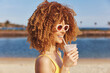 © SHOTPRIME STUDIO - Happy woman with curly hair enjoying a drink at the beach against a sunny background