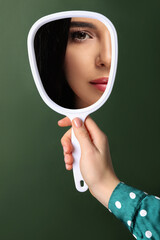 Canvas Print - Beautiful woman looking in handheld mirror on dark green background, closeup