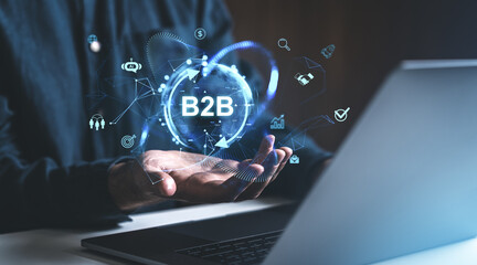 Poster - Business professional holding a glowing B2B icon with technology symbols on a digital interface in a modern workspace background.