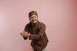 © Reezky - Joyful Indonesian man wearing lurik and blangkon smiling and shaking hands with guest.