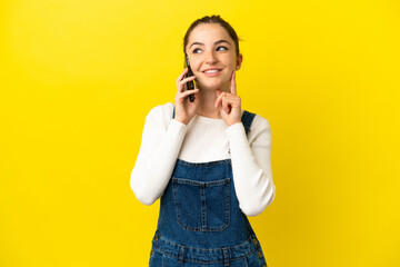 Wall Mural - Young woman using mobile phone over isolated yellow background thinking an idea while looking up