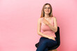 © luismolinero - Young woman sitting on a chair over isolated pink background pointing to the side to present a product