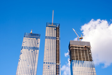 Poster - Three tall buildings with a crane on top of the middle one. The sky is blue and clear