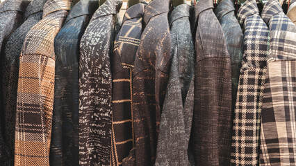 Poster - A row of plaid and checkered jackets hanging on a rack. The jackets are of different colors and patterns