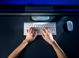 Aufkleber - Overhead view of hands typing on a white keyboard in dimly lit room at night.  A computer monitor and mouse are visible on a dark surface.