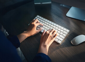 Aufkleber - Close-up of hands typing on a wireless keyboard at night.  Warm light illuminates the workspace, suggesting late-night work or focused effort.