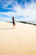 © Austockphoto - A woman stands high on a sand dune viewing into the distance of Moreton Bay.
