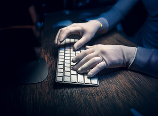 Aufkleber - Close-up of gloved hands typing on a keyboard in a dimly lit room.  The scene suggests secrecy or a clandestine operation.
