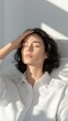 © Phisan - A serene portrait of a woman with closed eyes, resting gently with one hand on her forehead, bathed in soft natural light.