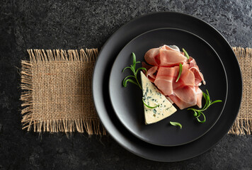 Wall Mural - Blue cheese, prosciutto, and rosemary on a black table.