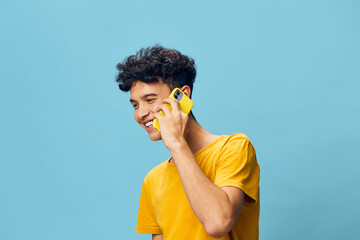 Wall Mural - Young man smiling while talking on the phone against a blue background, wearing a yellow t shirt, exuding a cheerful and relaxed vibe, perfect for lifestyle imagery