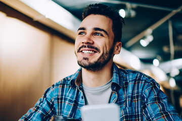 Wall Mural - cheerful handsome guy looking up imagine his vacation while chatting via smartphone in office, young