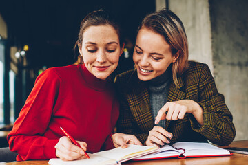 Fototapete - Successful two hipster girls drawing design sketch for new project teamworking in coffee shop.Cheerful friends writing down common plans of collaboration in notepad resting together in coworking
