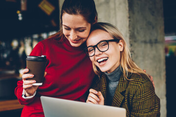 Fototapete - Portrait of happy blonde female blogger laughing at camera while having fun with best friend enjoying communication with each other and watching funny video on websites on laptop with 4G internet