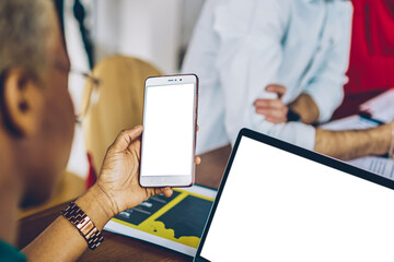 Fototapete - Cropped view of dark skinned young woman holding modern smartphone with blank screen and sharing media on laptop computer with mock up area via bluetooth connection.Female updating app on cellular