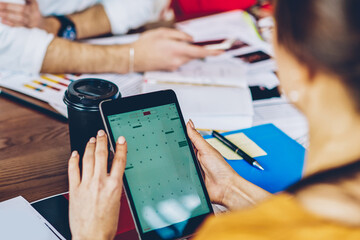 Fototapete - Cropped back view of young woman holding modern touch pad device in hands and searching app on internet website using wireless 4G connection during working process with colleagues in office