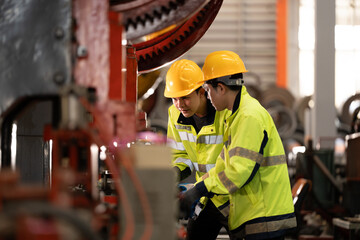 two professional engineer, worker, technician use clipboard discuss work, walk in steel metal manufacture factory plant industry.   Asian man and woman wear hard hat check quality machine.