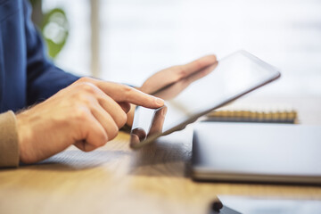 Poster - Closeup view of a male finger operating a high-tech tablet on a desk, set against the blurred backdrop of a luminous office scene