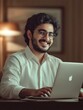 © Johannes - Smiling indian business man working on laptop at home office. Young indian student or remote teacher using computer remote studying, virtual training, watching online education webinar at home office