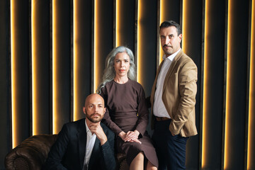 Aufkleber - Three professionals, including woman and two men, stand confidently in a contemporary office. The warm lighting and modern decor create an inviting atmosphere for collaboration.