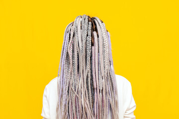 colorful dreadlocks and braids of a girl on a yellow isolated background back view, close-up of a wo