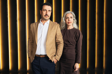Fototapete - Two European business professionals stand confidently against a stylish backdrop of illuminated vertical lines. They embody corporate leadership and management in a contemporary office environment.