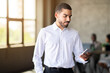 © Prostock-studio - A business professional checks his smartphone in a contemporary office environment. The warm lighting and diverse team in the background enhance the atmosphere of collaboration and productivity.