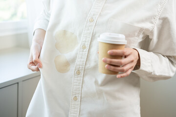 Wall Mural - Cloth stain, disappointment asian young woman clumsy with hot coffee, tea stains on shirt, hand show making spill drop on white shirt, spot dirty or smudge on clothes at home, isolated on background