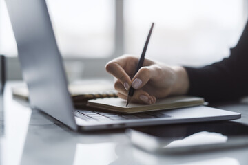 Poster - The close-up image showcases a woman's hand inscribing in a notepad on a modern laptop, with a soft-focus background