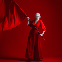 Rebel, a concept. The revolution. A woman in a red dress waves a huge red flag on a red background.