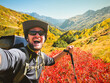 © Evaldas - Close up young happy caucasian excited active millennial man influencer take smartphone selfie while having fun on hiking trip outdoors reaching mountain peak destination. Beautiful autumn in Georgia