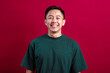 © Daniel - A cheerful young Asian man in a green T-shirt smiles warmly, standing confidently against a bold red background, exuding positivity and approachability in a relaxed and vibrant setting