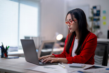 Wall Mural - A woman in a red jacket is typing on a laptop computer