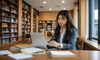 © RooftopStudioBangkok - focused Asian university student studies in library, using laptop surrounded by books and notes. serene environment enhances her concentration and learning experience