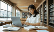 © RooftopStudioBangkok - Focused Asian university student studying in library, using laptop and taking notes. Surrounded by books, she embodies dedication and concentration in her academic pursuits