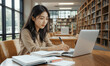 © RooftopStudioBangkok - focused Asian university student studies in library, using laptop and taking notes. serene environment enhances her concentration and learning experience