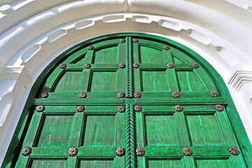 Wall Mural - Aged wooden door of bright green color with metal rivets and upper arch made of white stone - vintage architecture background with old wooden door