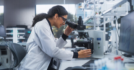 Poster - Close Up Portrait of a Latin Female Microbiologist Wearing Safety Glasses and Looking Through the Microscope, Analyzing Sample Cells. Skillful Scientist Working in a Medical Science Laboratory