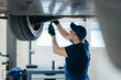© andrew_shots - Young car mechanic at repair service station inspecting car wheel and suspension detail of lifted automobile