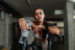 © DusanJelicic - In a stylish gym setting, a fit woman poses for a photo after an intense air bike workout, demonstrating both fitness and self-confidence.