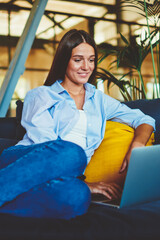 Fototapete - Positive smiling hipster girl searching comedy show for watching using modern laptop device indoors, happy woman resting on comfortable sofa while messaging with friends via application on netbook