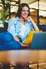 Fototapete - Happy successful woman enjoying shopping via laptop device connected to wifi at comfortable campus, smiling hipster girl in denim look watching positive movie using wireless internet on modern netbook